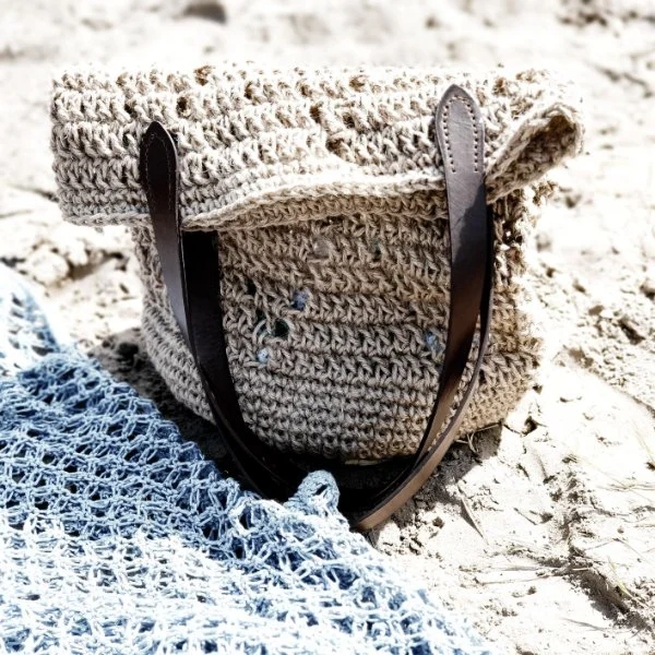 a beach bag with leather handles on the sand.