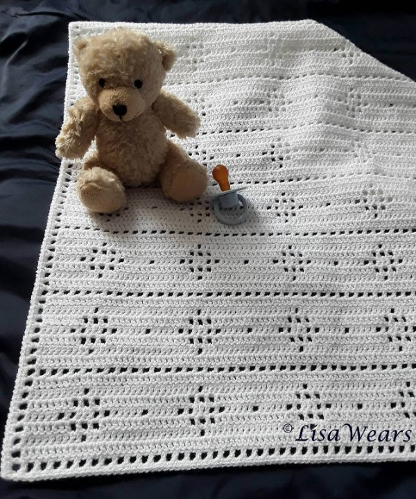 A teddy bear sitting on a white filet crochet blanket.