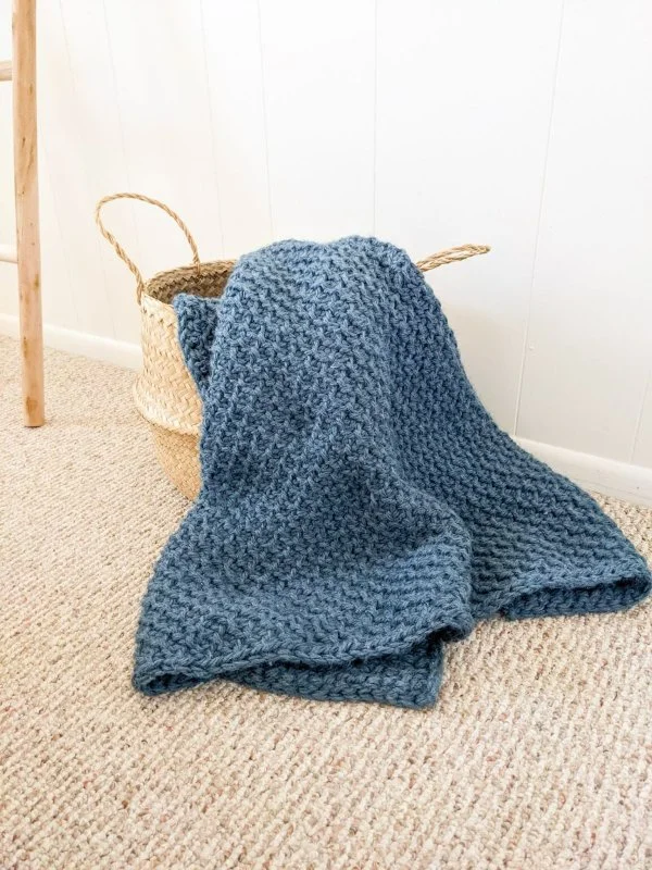 A blue Tunisian crochet baby blanket draped over a basket.