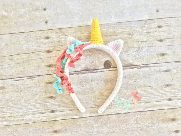 A unicorn-themed crochet headband on a wooden board backgorund.