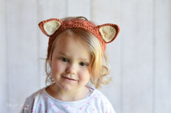 A toddler wearing a crochet fox headband.