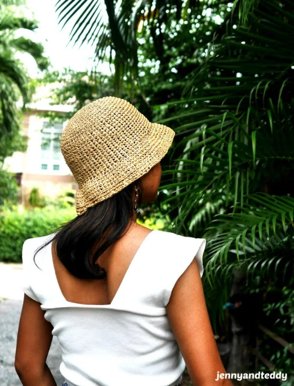 A woman in a tropical garden wearing a crochet raffia bucket hat.