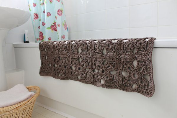 A granny square motif crochet bath mat hanging over a bath.