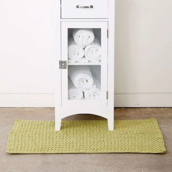 A white cabinet holding towels and a green crochet bath mat.