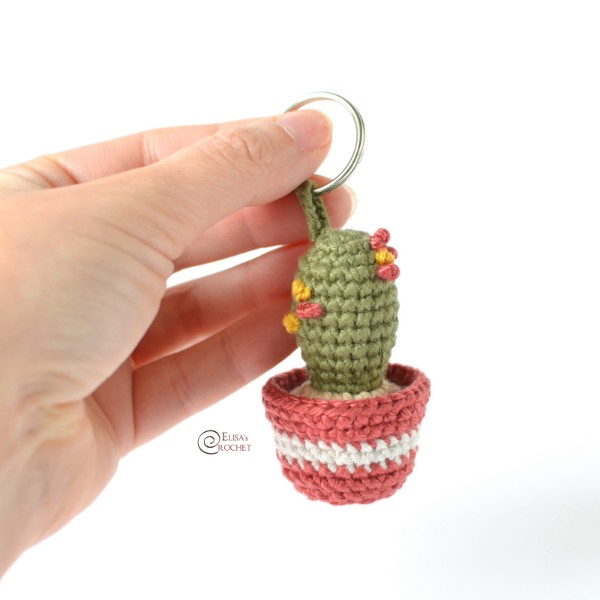 A little crochet cactus keychain in held in a hand.