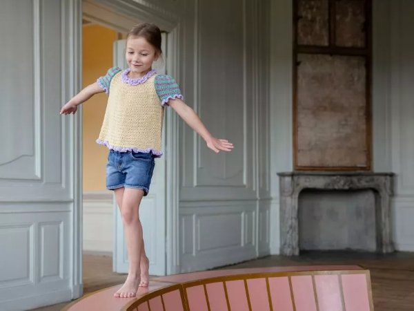 A child balancing and wearing a multi-coloured kids' crochet tee.