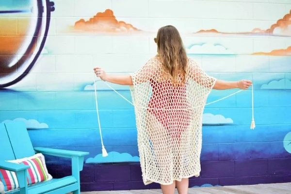 A woman in a white crochet beach cover-up standing in front of a beach mural.