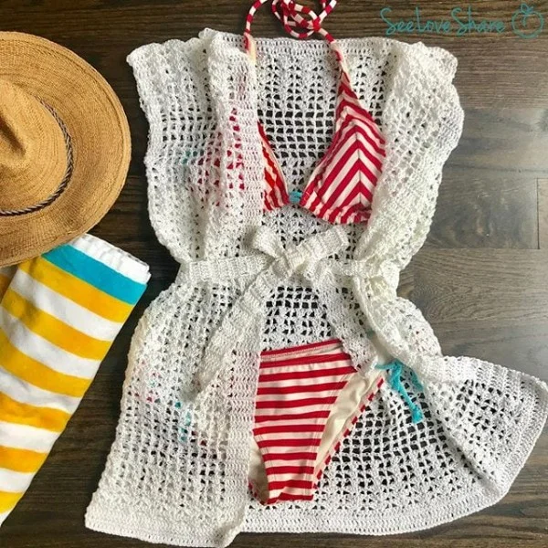 A flatlay image of a crochet beach cover-up and a red and white bikini.
