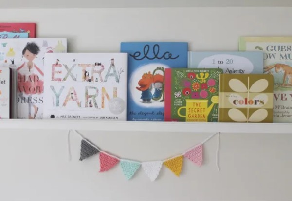 A crochet bunting hanging under a sehlf with childrens books.