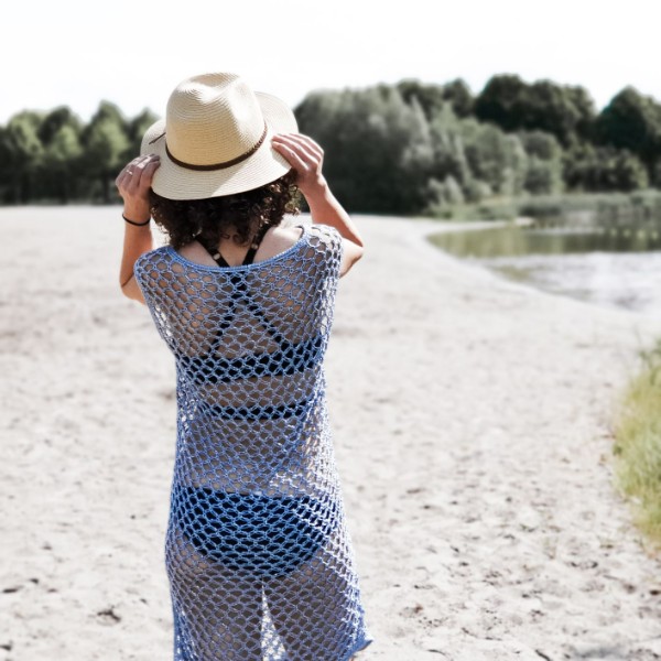 Back view of a woman on a beach wearing a hat and a blue crochet cover-up.