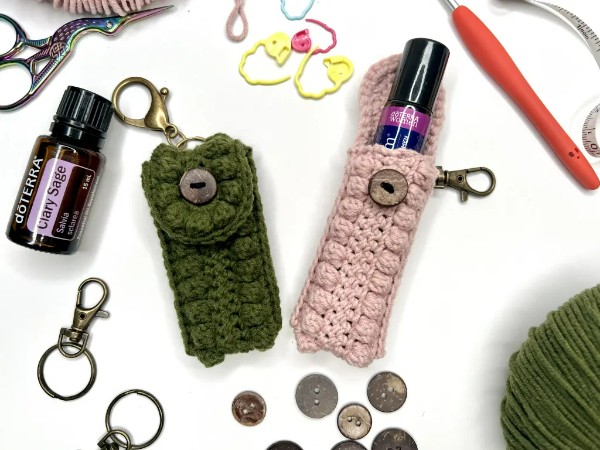 Tw crochet essential oil holder keychains with buttons and stitch markers in the background.