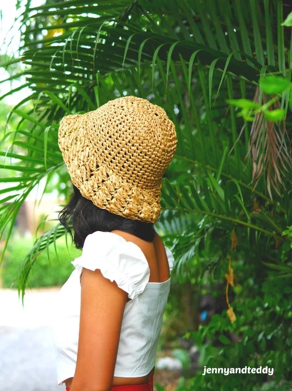 A woman in a tropical garden wearing a crochet raffia sun hat.
