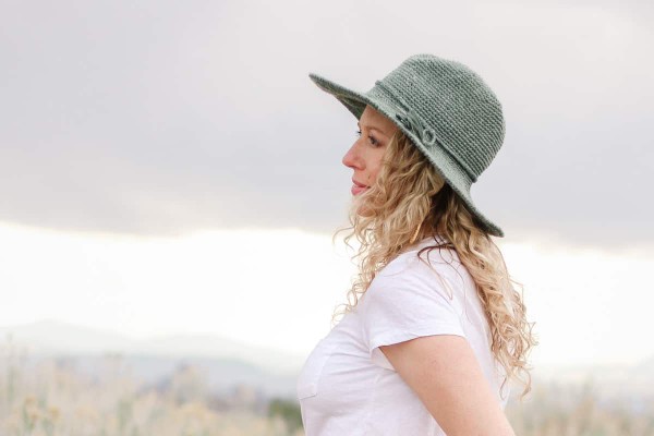 A side view of a woman outdoors, wearing a fedora-style crochet sun hat.