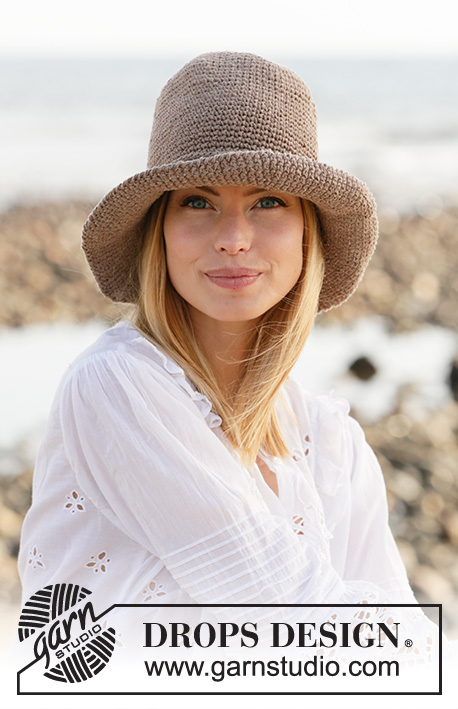 A closeup of a woman on a rocky beach wearing a crochet sun hat.