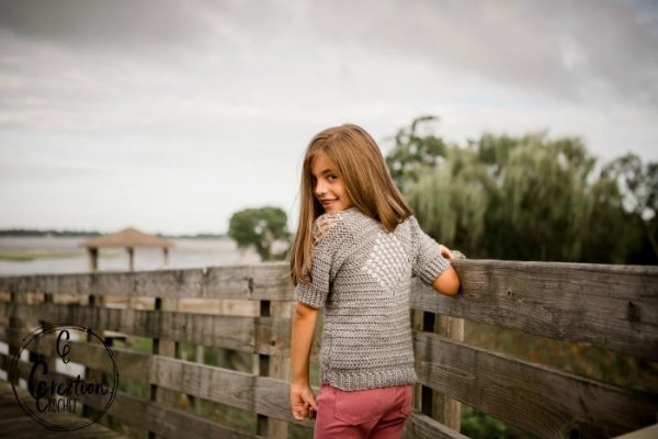 A girl outdoors weraing a grey crochet t-shirt with a lacy diamond back panel.