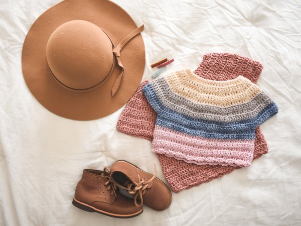 A flat lay of two kids' crochet t-shirts with a hat and shoes.