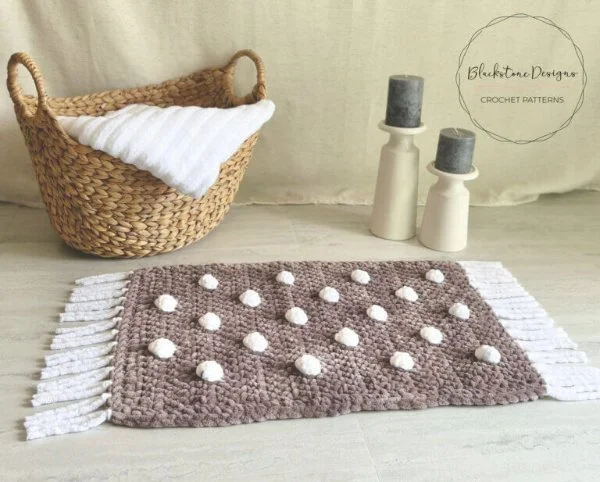 A brown and white crochet bath mat with a basket and towel.