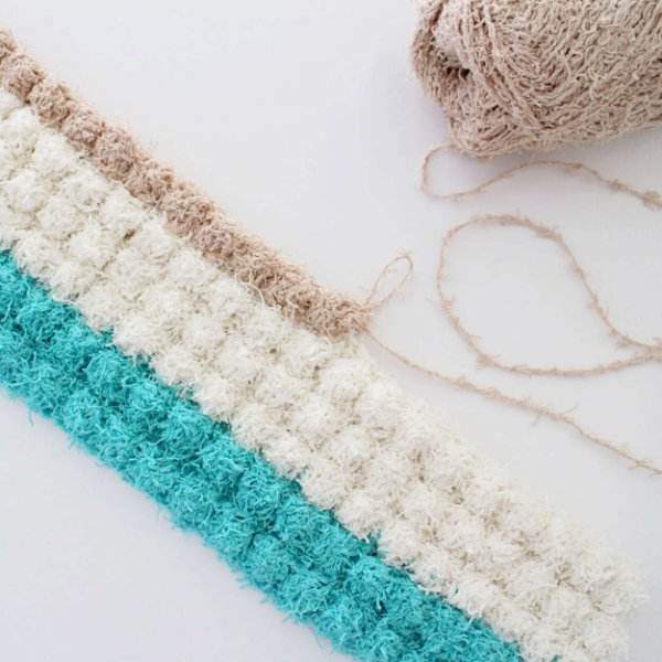 An incomlete crochet bathmat in bobble stitch with yarn and a hook.