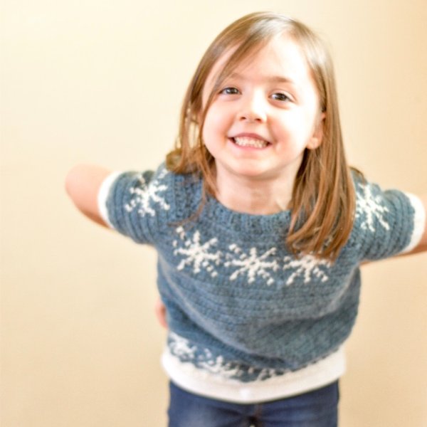 A girl wearing a blue and white crochet t-shirt with snowflake motifs.