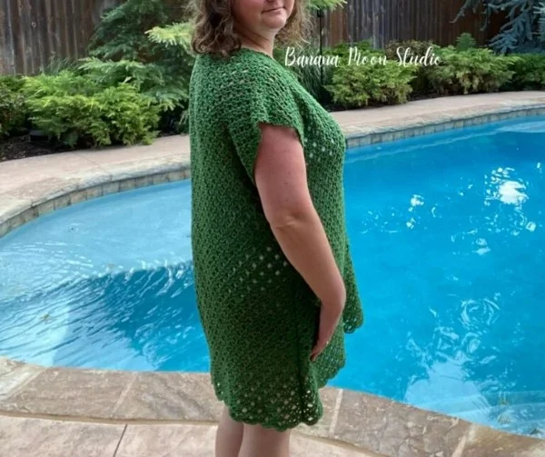 A woman standing by a pool wearing a green crochet swim cover.