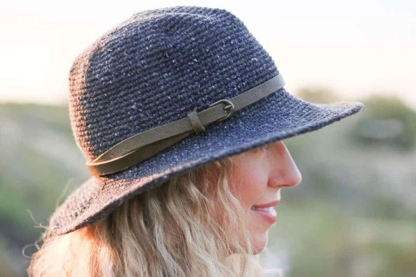 A side view of a woman outdoors wearing a blue rancher-style crochet sun hat with a leather hat band.
