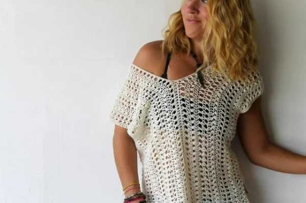 A woman wearing a lacy white off shoulder crochet beach cover-up.