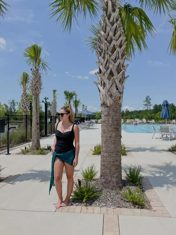 A woman by a pool wearing a crochet sarong over a swim suit.