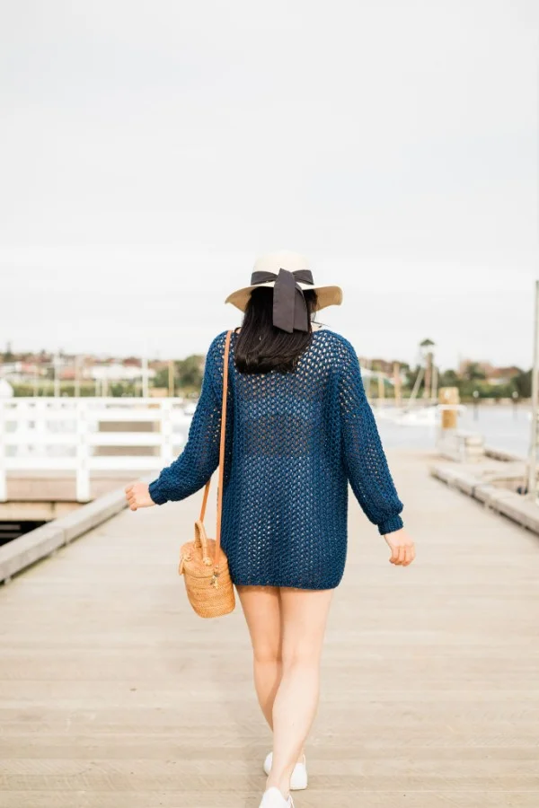 A woman walking along a pier wearing a navy blue crochet cover-up.
