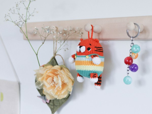 A keychain with a  crochet tiger wearing striped overalls hanging from a hook.