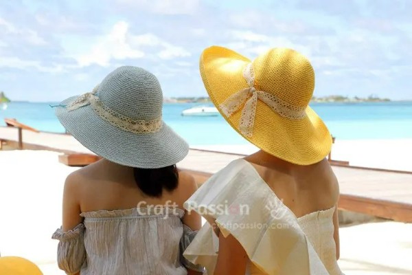 Two women on a beach wearing wide-brimmed crochet sun hats