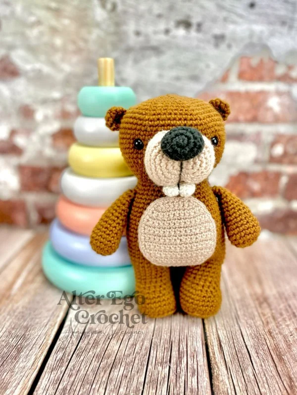 A crochet beaver standing in front of toy rings.