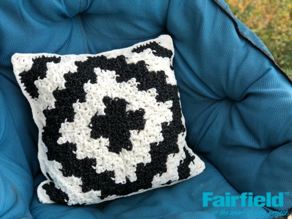 Black and white C2C crochet pillow on a blue chair.