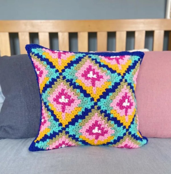 A colourful C2C crochet cushion on a bed.