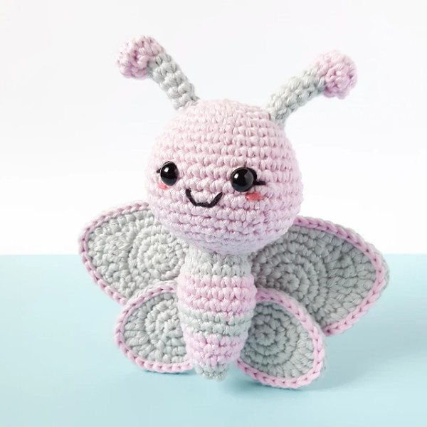 A pink and grey pastel crochet butterfly toy.