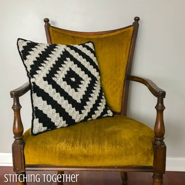 A black and white c2c crochet pillow on a yellow velvet chair.