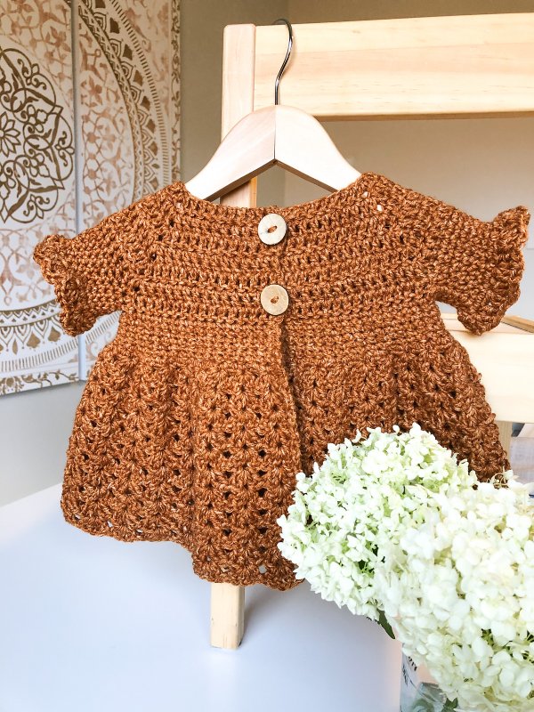 Lacy crochet baby cardigan on a hanger.