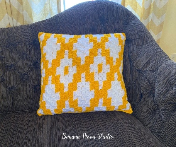 A yellow and white geometric crochet corner-to-corner pillow on a blue chair.