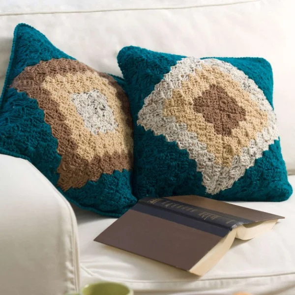 Two geometric corner-to-corner crochet pillows on a lounge.