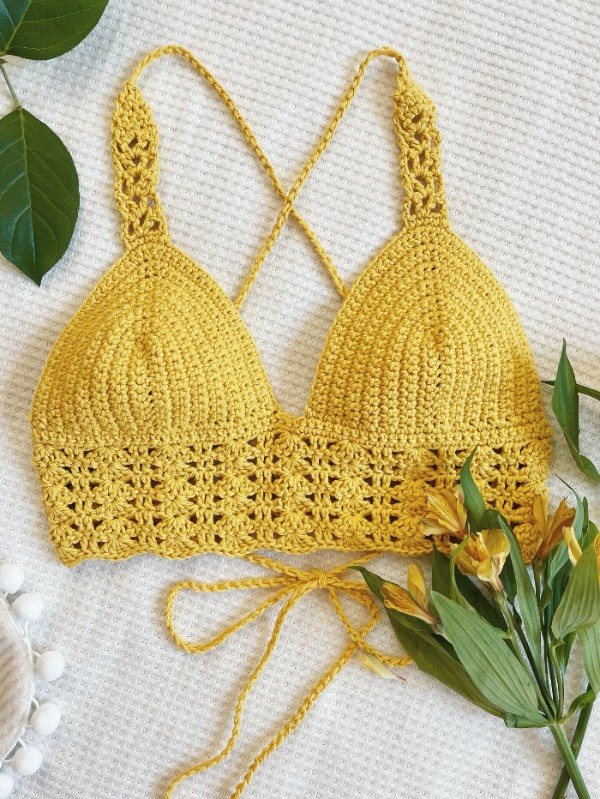 A yellow crochet bralette on a white background with greenery.