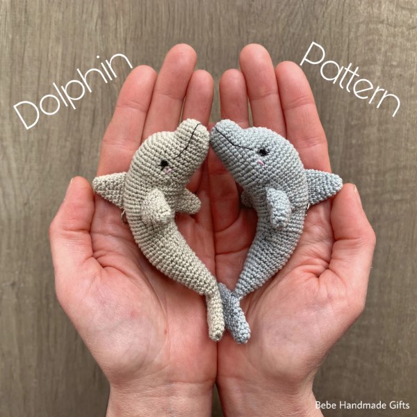 Two small crochet dolphin amigurumi in the palms of someones hands.