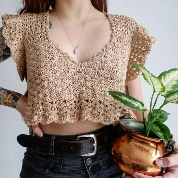 A closeup of a woman weraing a lacy cropped crochet top with ruffled hem.