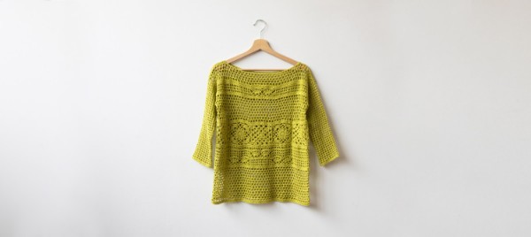 A lime green crochet lace top on a wooden clothes hanger.