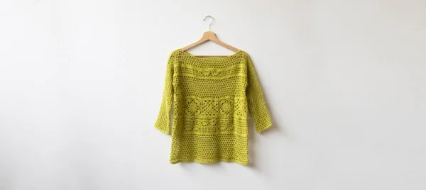 A lime green crochet lace top on a wooden clothes hanger.