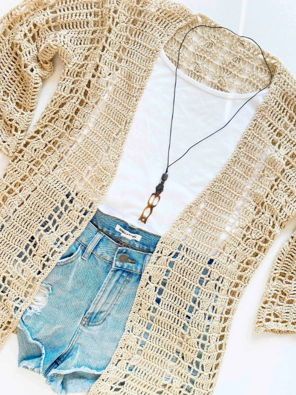 A flat lay image of a lacy crochet cardigan, a white tee, and jeans shorts.