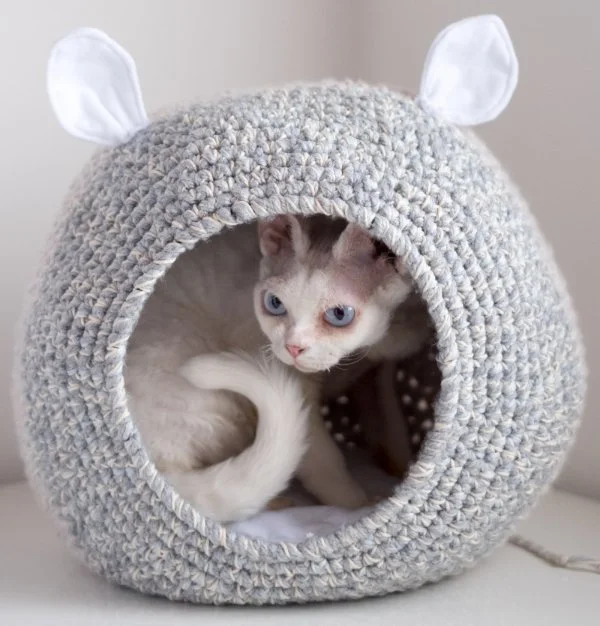 A cat in a crochet cat cave with ears.