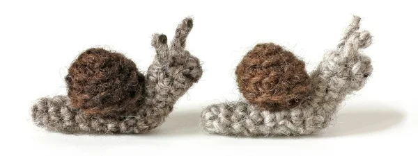 Two little crochet snail amigurumi in brown tones.