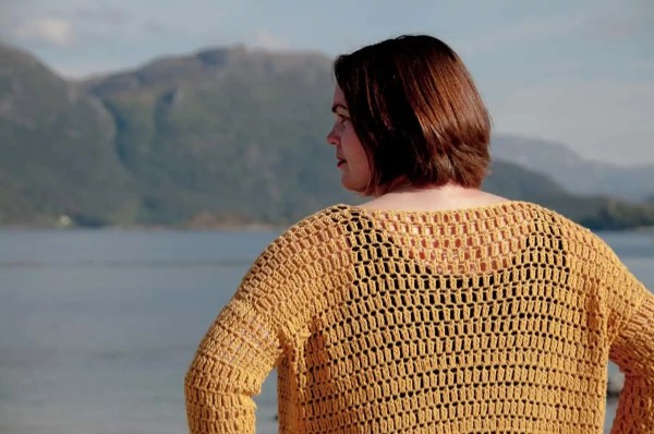 A close up back view of a woman weraing a crochet lace cardigan.