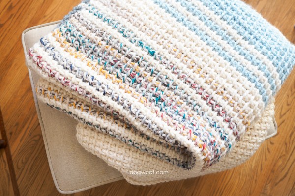 A striped Tunisan crochet blanket folded on a stool.