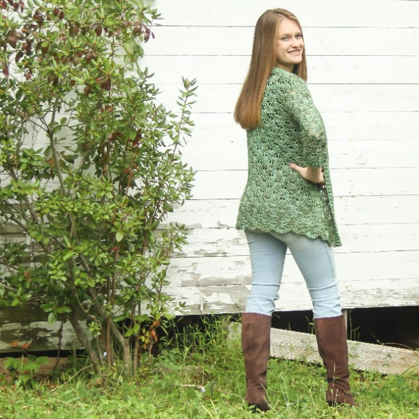 A woman waering a green crochet lace cardgian with jeans and boots.