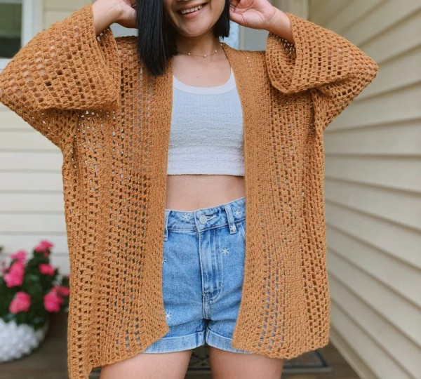 A woman wearing an oversized crochet lace cardigan with jeans shorts.